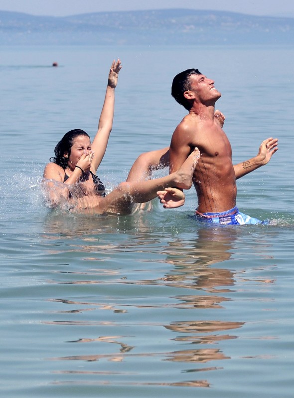 Fiatal lány ugrik a vízbe egy fiú hátáról a Balatonban, a siófoki Aranyparton