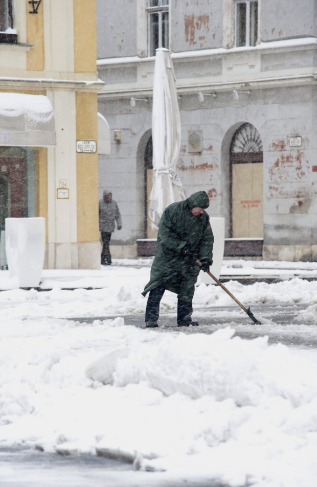 Egy férfi havat lapátol Győrben  